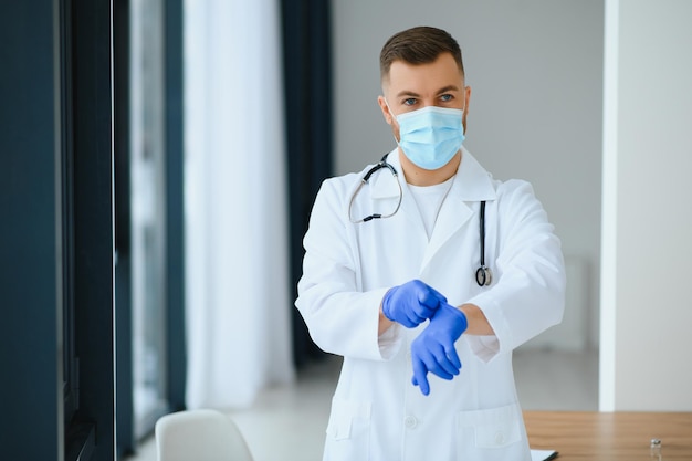 Portret van mannelijke arts met chirurgisch masker staat klaar om patiënten met coronavirus of covid-virus te helpen.