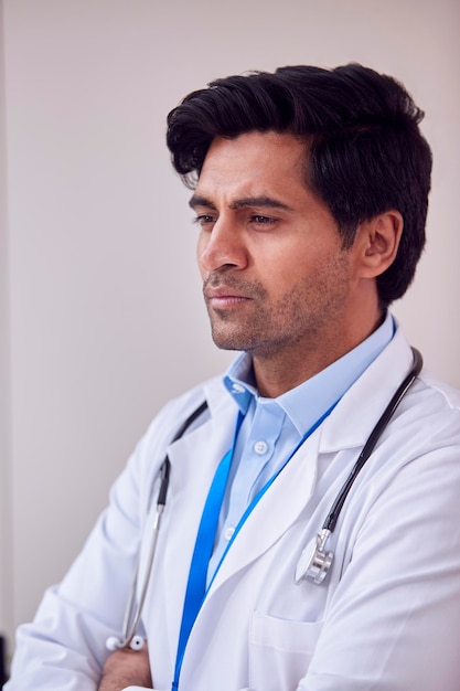 Portret van mannelijke arts of huisarts met een stethoscoop die een witte jas draagt die in het kantoor staat