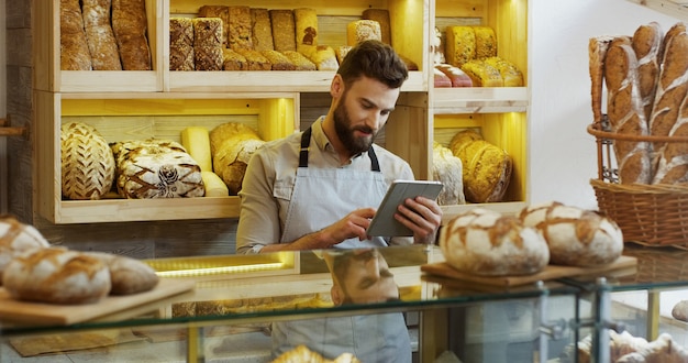 Portret van mannelijke bakker die in bakkerijwinkel werken en tablet gebruiken