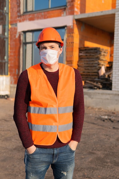 Portret van mannelijke bouwvakker met medisch masker en overall op de achtergrond van een huis in aanbouw