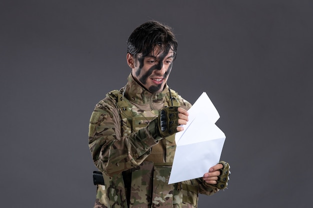 Portret van mannelijke soldaat in camouflage blij met brief van familie donkere muur