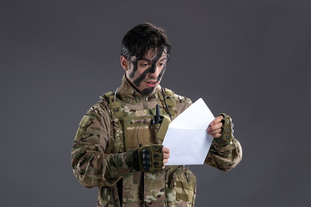 Portret van mannelijke soldaat in camouflage die brief leest van familie op donkere muur