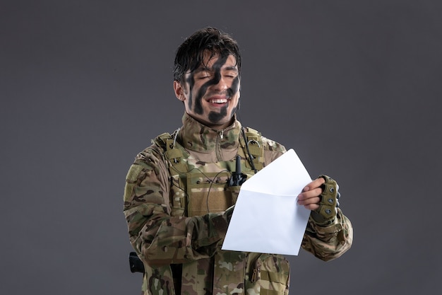 Portret van mannelijke soldaat in camouflage die brief leest van familie op donkere muur