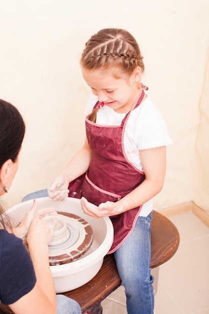 Portret van meisje dat aardewerk probeert te maken van witte klei op een pottenbakkersschijf