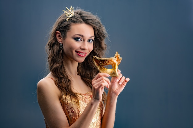 Portret van meisje die speels de camera met een prinseskroon bekijken op haar hoofd en in een gouden kleding.