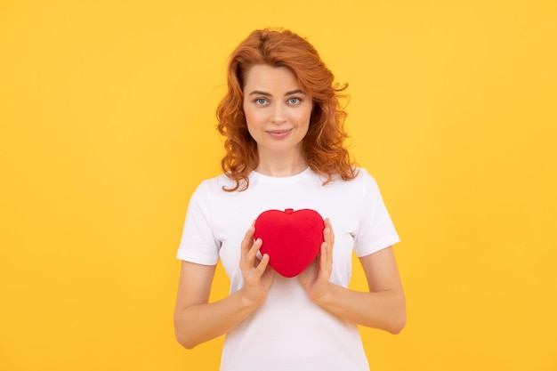 Portret van meisje met hart. fijne Valentijnsdag. wees mijn Valentijn. dame op gele achtergrond. liefde aanwezig. lachende roodharige vrouw met liefde romantisch cadeau. schatje. Valentijns verkoop.