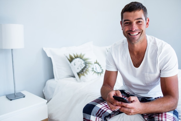 Portret van mensenzitting op bed en het typen van een tekstbericht op telefoon