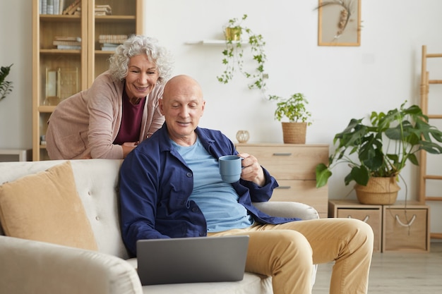 Portret van moderne senior paar glimlachen naar laptop camera tijdens videogesprek met familie