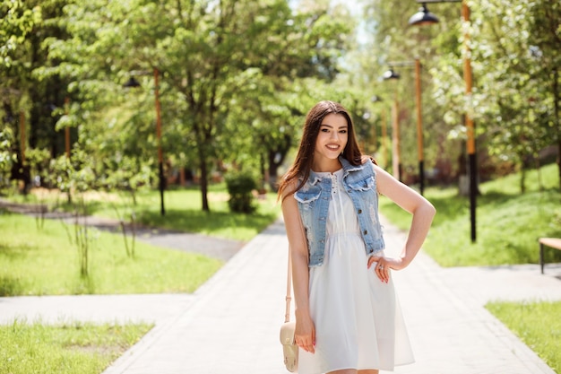 Portret van modieuze blanke vrouw tijd buiten doorbrengen in het park in de zomer. Het meisje is gekleed in witte kleding en denimvest.