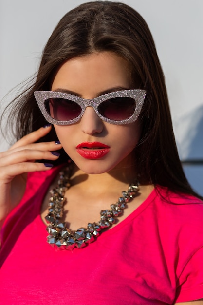 Portret van modieuze brunette vrouw in stijlvolle zonnebril en roze t-shirt close-up