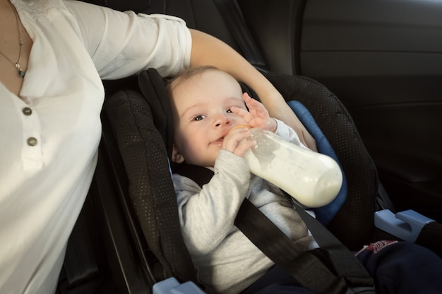 Portret van moeder die baby in auto uit fles voedt