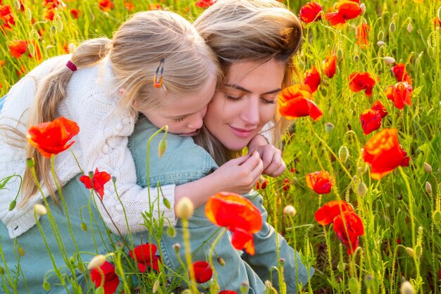 Portret van moeder en dochter die door een bloeiende familievakantie in de zomer van een papaverveld lopen op na