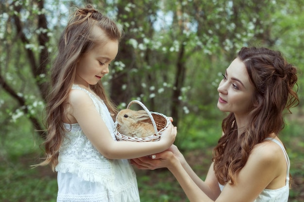 Foto portret van moeder en dochter in het bos in de handen van het meisje een mand met een konijn