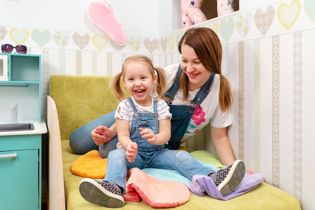 portret van moeder en lachende dochter zittend op het bed in de kinderkamer