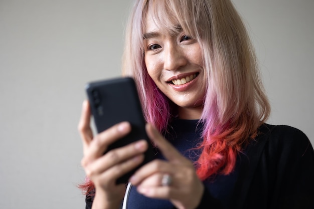 Portret van mooi Aziatisch stijlvol trendy meisjesmodel met smartphone in casual zomerkleren pastelroze en rood haar