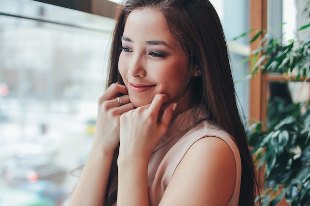 Portret van mooi charmant romantisch brunette glimlachend Aziatisch meisje dichtbij het venster bij koffie