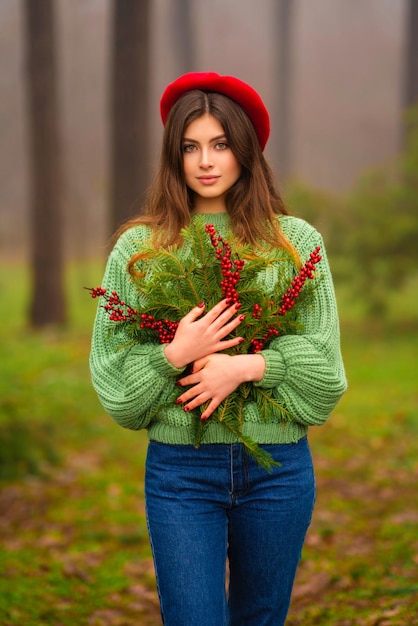 Portret van mooi donkerbruin meisje in rode hoed en groene gebreide trui met kersttakken