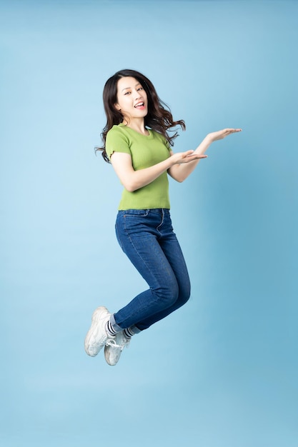 Portret van mooi jong Aziatisch meisje dat omhoog springt, geïsoleerd op blauwe achtergrond