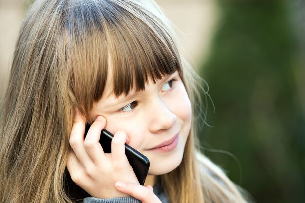 Portret van mooi kindmeisje met lang haar dat op celtelefoon spreekt. kleine vrouwelijke jongen communiceren via smartphone. kinderen communicatieconcept.