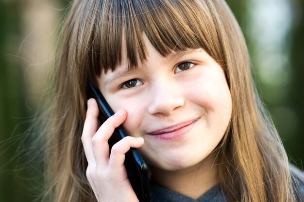 Portret van mooi kindmeisje met lang haar dat op celtelefoon spreekt