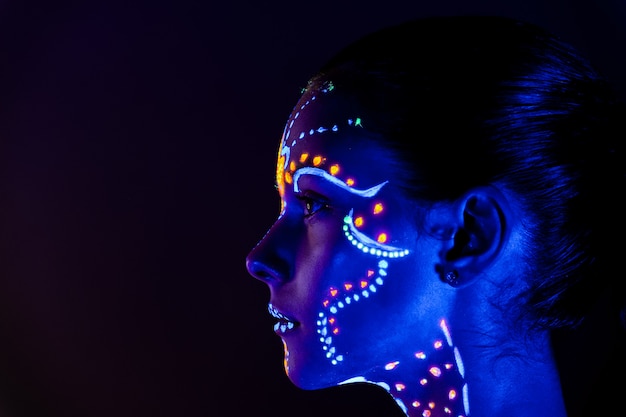 Portret van mooi meisje met ultraviolette verf op haar gezicht. Meisje met neon make-up in kleur licht.