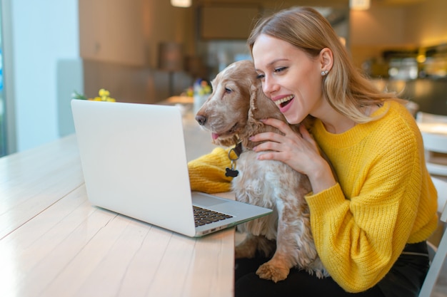 Portret van mooi meisje met verrast gezicht dat haar aanbiddelijk puppy houdt en laptop met behulp van