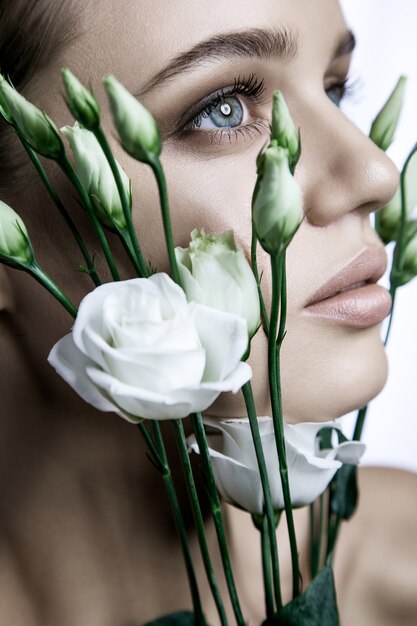 Portret van mooi model met goede huid op witte achtergrond met witte rozen bloem.