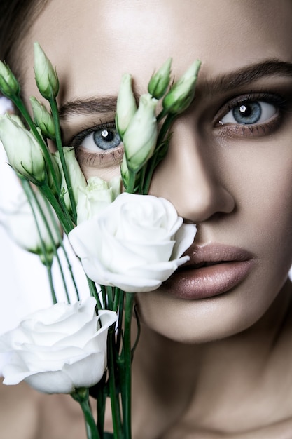 Portret van mooi model met goede huid op witte achtergrond met witte rozen bloem.
