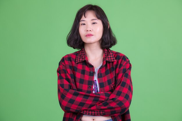 Portret van mooie Aziatische hipster vrouw met kort haar tegen Chromakey of groene muur