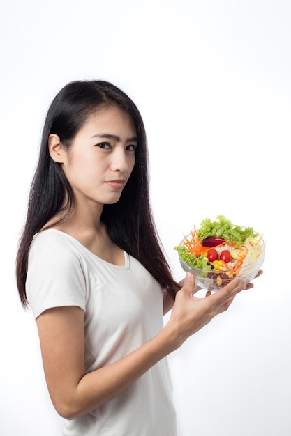 Foto portret van mooie aziatische jonge vrouw die groentesalade eet die op witte achtergrond wordt geïsoleerd.