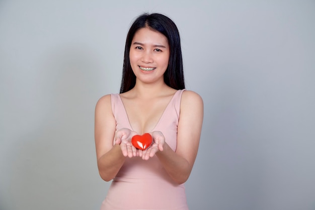 Portret van mooie Aziatische jonge vrouw met wijzende rode hart vorm geïsoleerd op lichtgrijze achtergrond met kopie ruimte