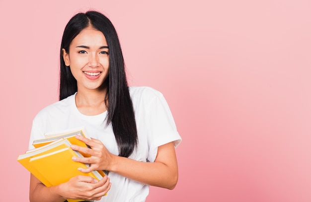 Portret van mooie Aziatische jonge vrouw tiener glimlachend knuffelen boeken, vrouwelijke houder boek multicolor, studio opname geïsoleerd op roze achtergrond met kopie ruimte, onderwijs concept