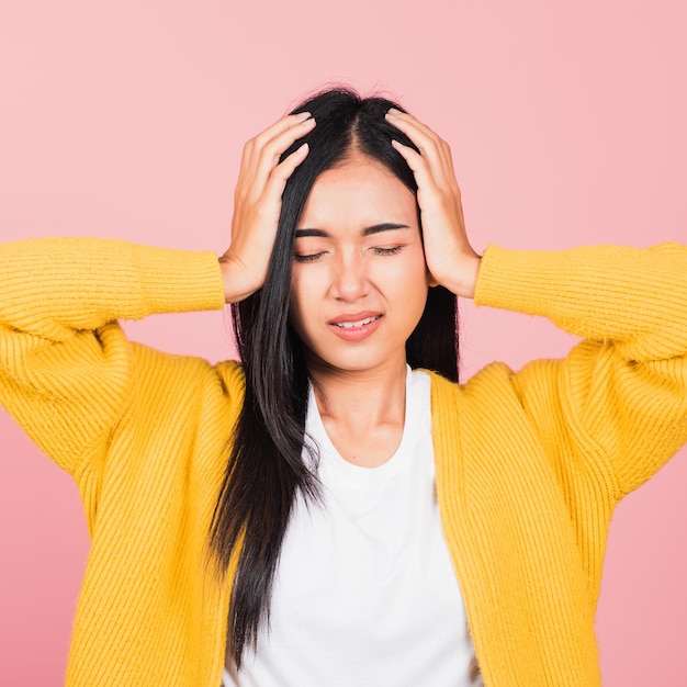 Portret van mooie Aziatische jonge vrouw verdrietig moe spanning gezicht houden hoofd vasthouden door handen, vrouwelijke persoon gesloten ogen probleem ze hoofdpijn, studio opname geïsoleerd op roze achtergrond