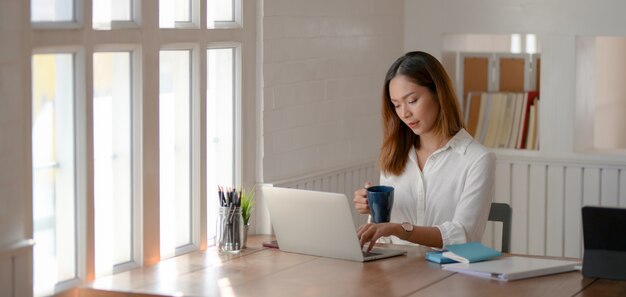 Portret van mooie Aziatische onderneemster die aan haar project werkt en een koffie drinkt