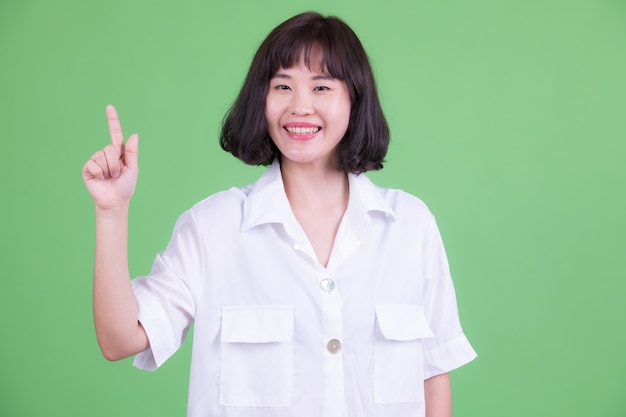 Portret van mooie Aziatische onderneemster met kort haar tegen Chromakey of groene muur