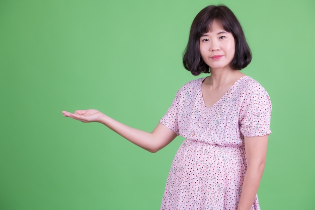 Portret van mooie Aziatische zwangere vrouw met kort haar tegen Chromakey of groene muur