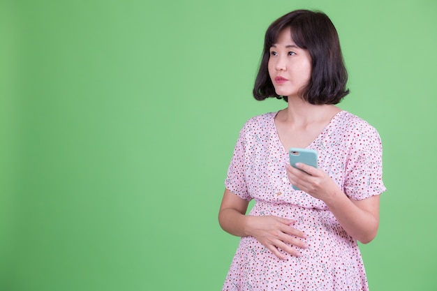 Portret van mooie aziatische zwangere vrouw met kort haar tegen chromakey of groene muur