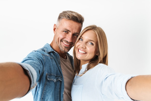 Portret van mooie blanke paar man en vrouw in basiskleding glimlachend en selfie foto samen geïsoleerd op wit