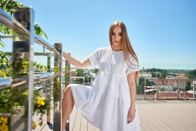 Portret van mooie blonde model in zomer witte jurk. meisje poseren op het dak van het huis.