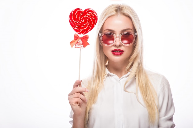 Portret van mooie blonde vrouw met heldere make-up en rood in hand suikergoedhart