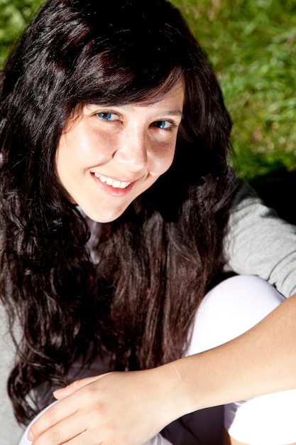 Portret van mooie brunette meisje met blauwe ogen op groen gras in het park.