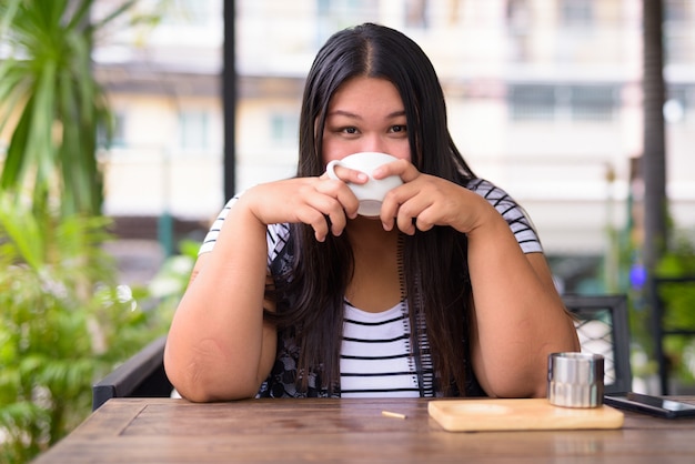 Portret van mooie dikke Aziatische vrouw ontspannen in de koffieshop