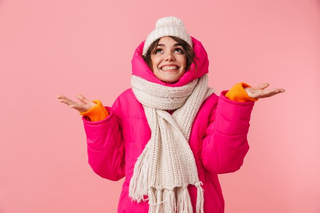 Portret van mooie gelukkige vrouw in warme kleren glimlachend met handen geïsoleerd op roze