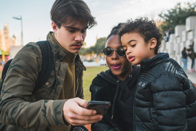 Portret van mooie gemengd ras etnische familie plezier, ontspannen en met behulp van mobiele telefoon in het park buiten.