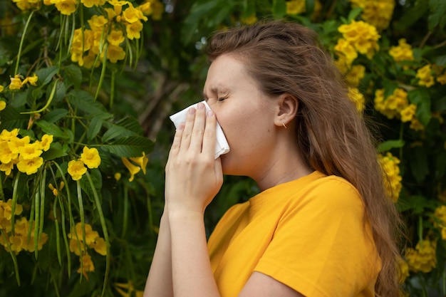 Portret van mooie jonge allergische vrouw lijdt aan pollenallergie of verkoudheid op natuurlijke bloem bloeiende boomachtergrond in de lente of zonnige zomerdag niest terwijl ze haar loopneus snuit en in de ogen wrijft