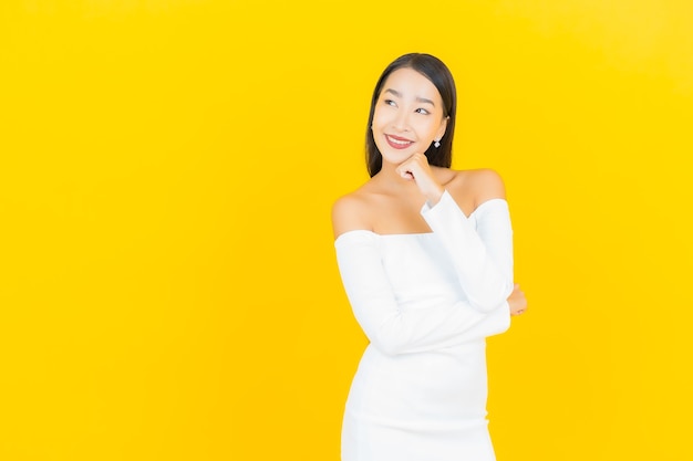 Portret van mooie jonge bedrijfs Aziatische vrouw die met witte kleding op gele muur glimlacht