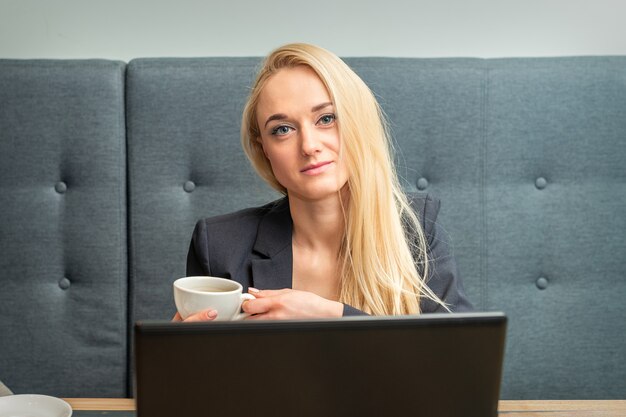 Portret van mooie jonge blanke zakenvrouw met kopje koffie in kantoor