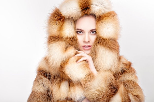 Portret van mooie jonge blonde vrouw in de bontjas van de luxevos. wintermode op grijze achtergrond