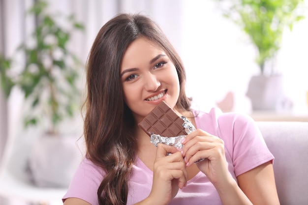 Portret van mooie jonge brunette met chocolade op de bank in de kamer close-up