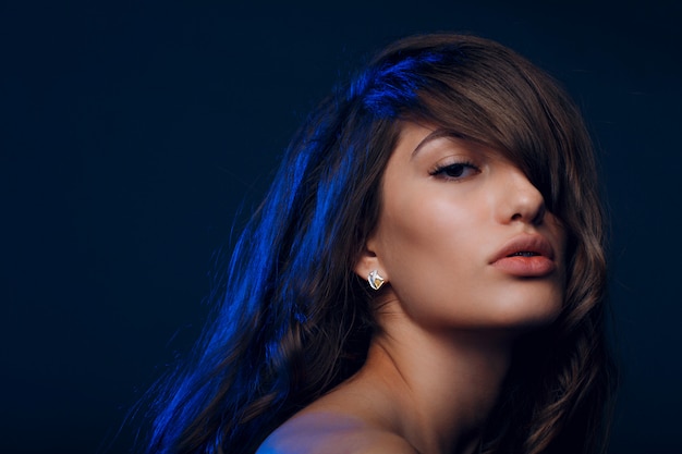 Portret van mooie jonge brunette vrouw met gezond haar in blauw licht